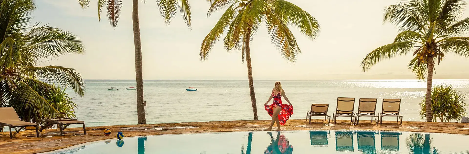 Woman in a red dress walking around a swimming pool surrounded by palm trees on a tropical vacation in Zanzibar, Tanzania | Go2Africa