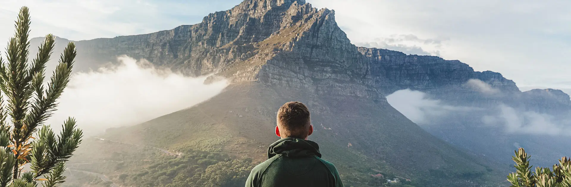 A man faces away from the camera looking at the edge of Table Mountain in Cape Town from an elevated position | Go2Africa