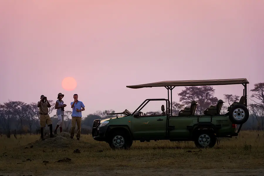 Guests enjoy sundowners during a game drive near linkwasha camp in hwange, zimbabwe